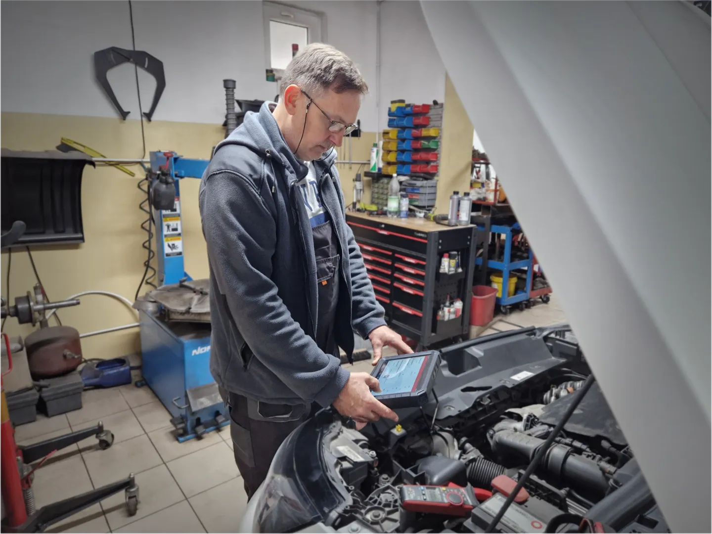 Mechanik korzysta z testera diagnostycznego przy otwartej masce samochodu w AutoControl.